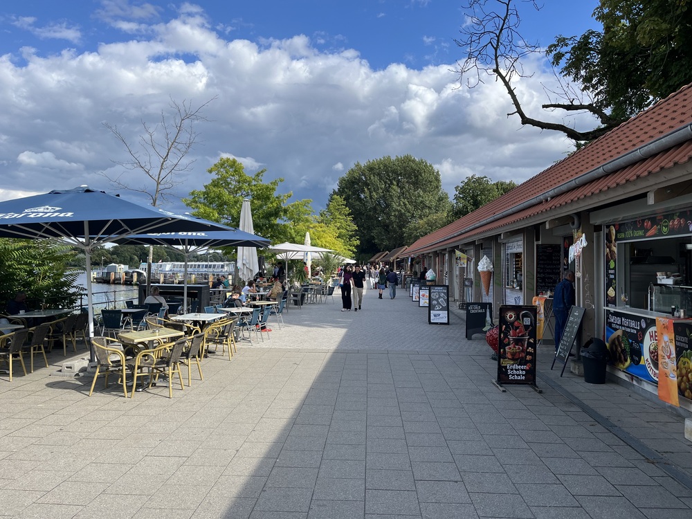 Mehrere Essensstände mit Tischen, Stühlen und Markisen am Hafen Treptow
